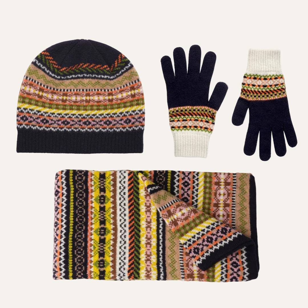 Lambswool winter accessory set on a white background, including a beanie, a pair of gloves, and a scarf, all featuring a multicolor Fair Isle pattern with navy, cream, yellow, orange, and black.