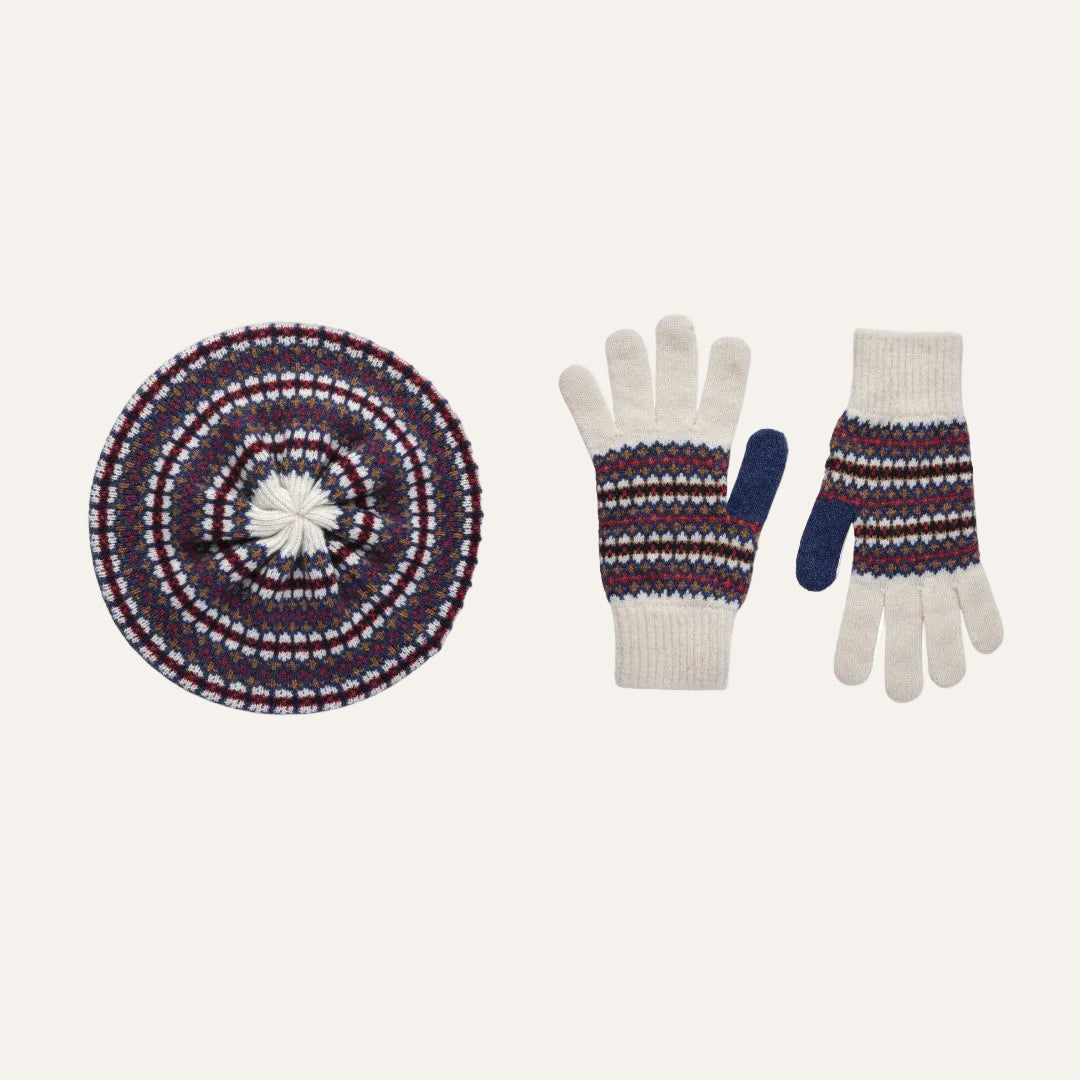 A knit winter accessory set on a plain white background, featuring a round lambswool beanie hat with concentric Fair Isle patterns and a pair of knit gloves with matching patterned cuffs and blue thumb sections.