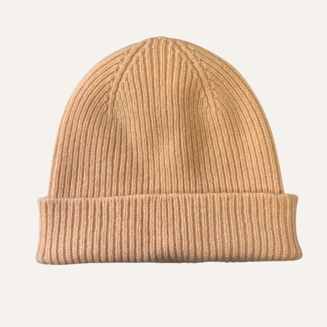 A classic ribbed knit beanie hat in a warm peach color, shown flat against a solid white background.