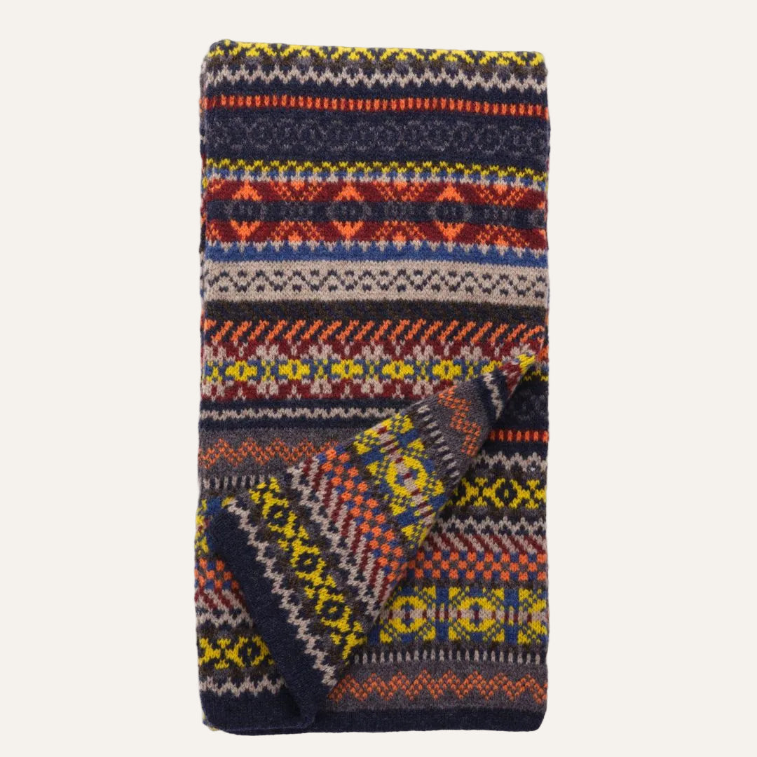A knit scarf featuring a multicolor Fair Isle pattern with navy, red, yellow, beige, and gray stripes and geometric motifs, shown on a plain white background.