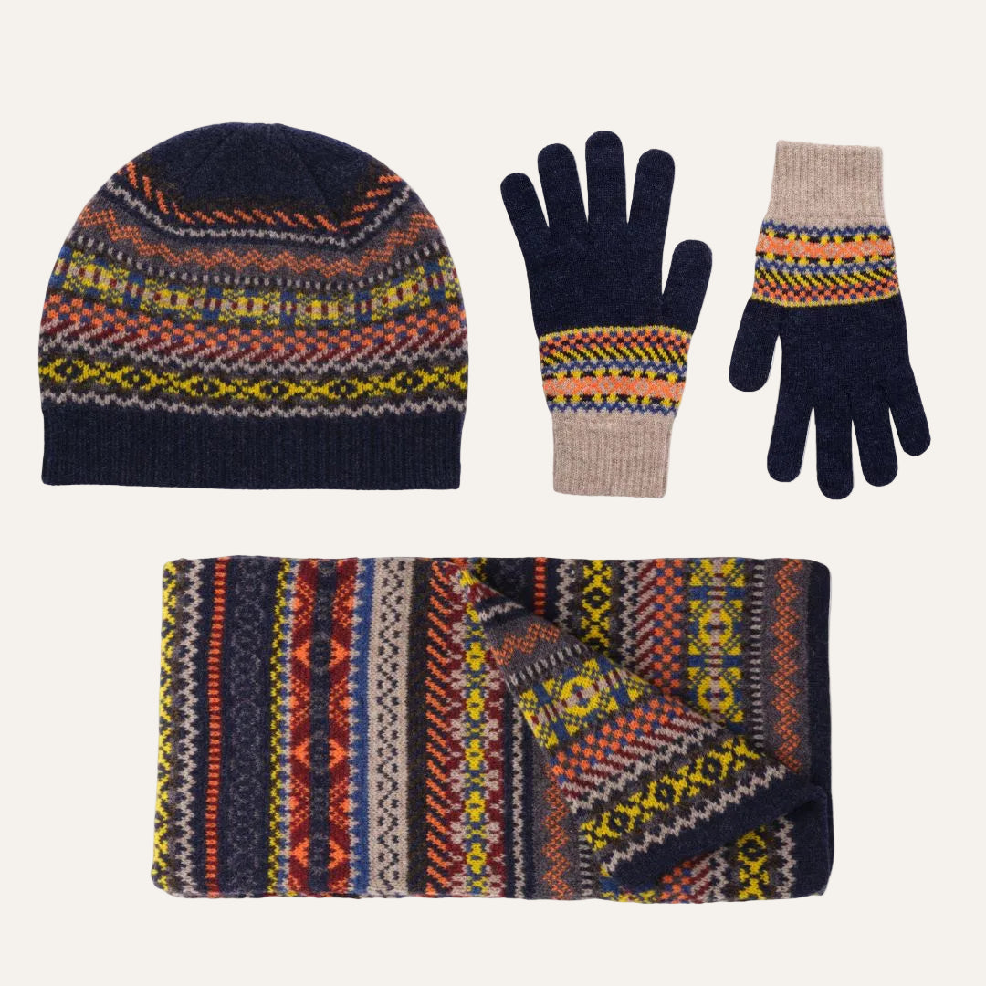 Lambswool knit winter accessory set on a white background, including a beanie, gloves, and a scarf, all featuring a multicolor Fair Isle pattern with navy, orange, yellow, red, and beige.