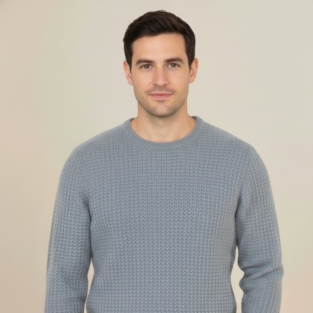 Man wearing a light grey cashmere honey comb knitted sweater against a plain background