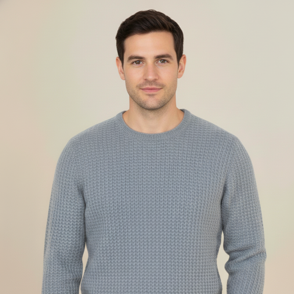 Man wearing a light grey cashmere honey comb knitted sweater against a plain background
